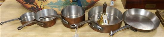 A set of four graduated copper saucepans and a frying pan and a brass bell with turned wood handle